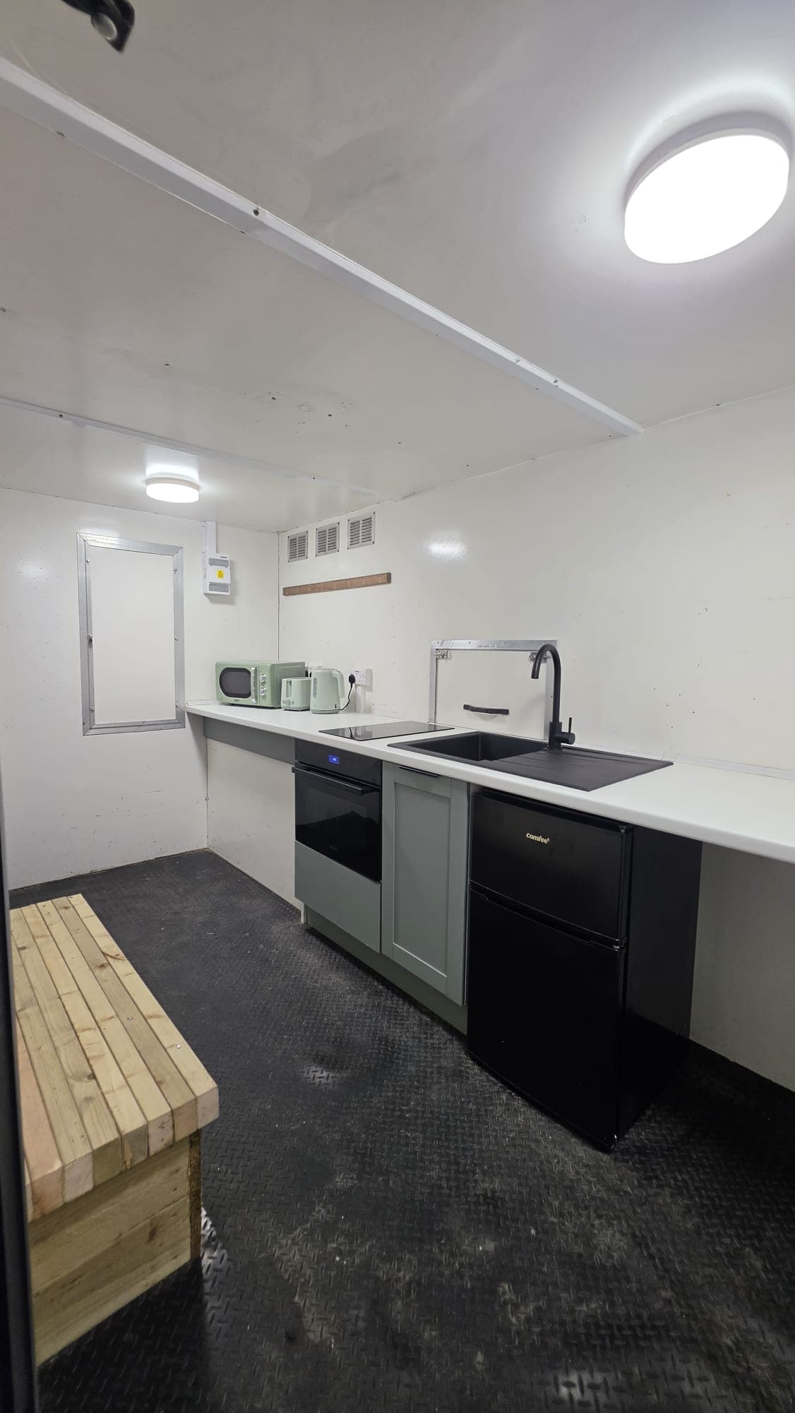 Tall view of the fitted kitchen, with light on and cabinets in sage green.