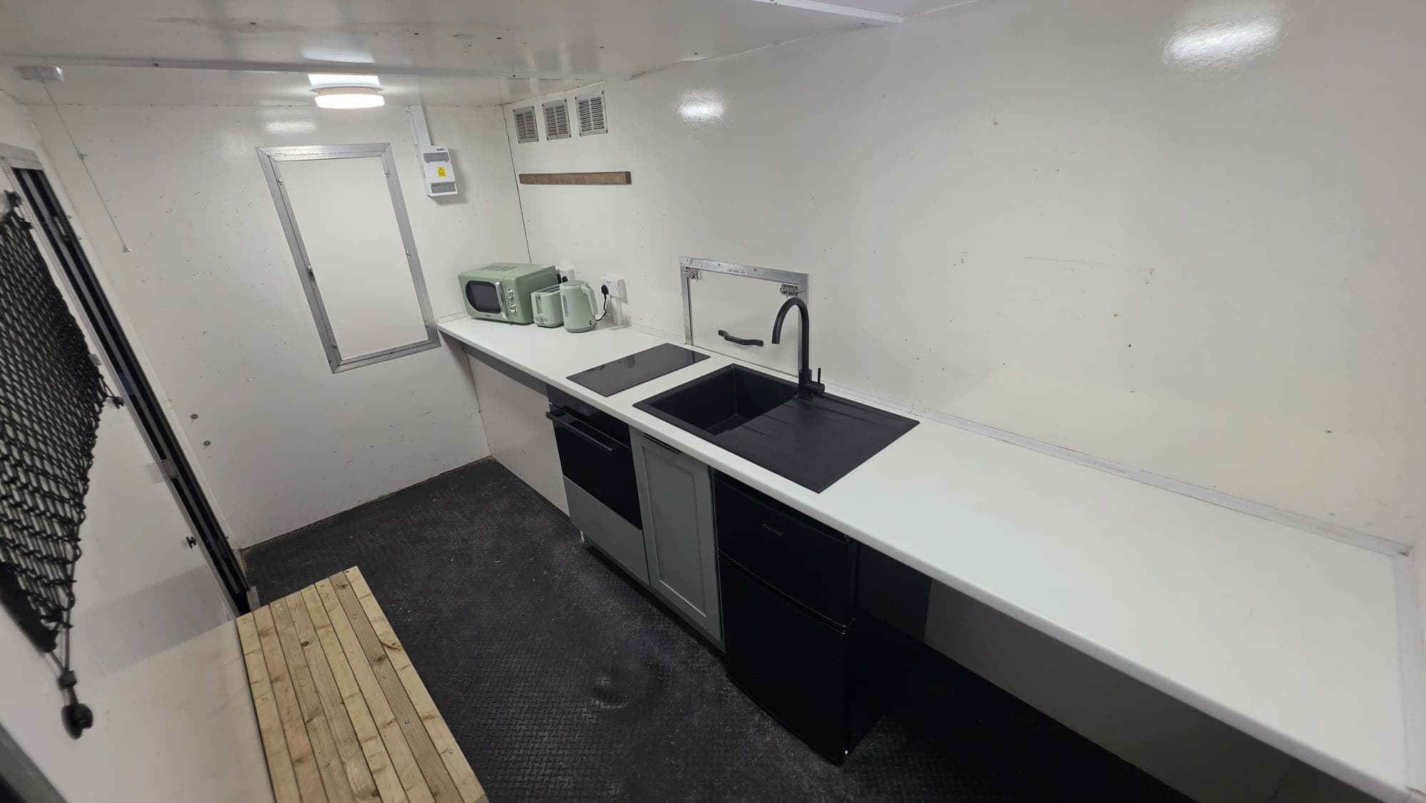 Wide view inside the trailer with worktop, sink, hob, oven and fridge along one wall.